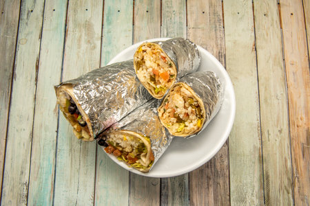 Two huge burritos halved and rolled with aluminum foil on a white bowlの写真素材