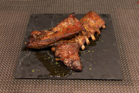 Delicious barbecued ribs seasoned with parsley, pepper, garlic and salt on a square black slate plateの写真素材