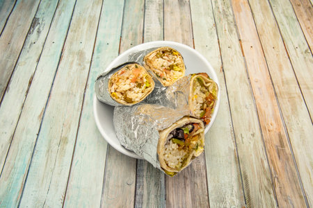 white bowl with large halves of maxi burritos of different variants on wooden tableの写真素材