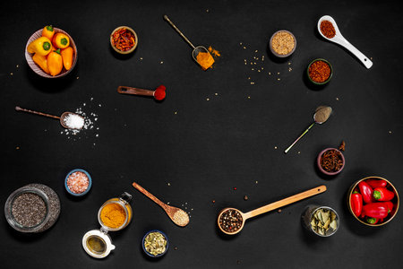 Top view of spoons and bowls filled with all kinds of spices and condiments on black backgroundの写真素材