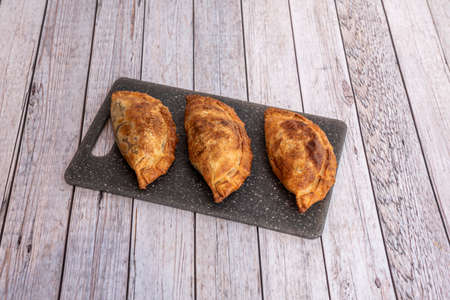 Popular Argentine empanadas stuffed with stewed beef and the dough well toasted on a black plateの写真素材