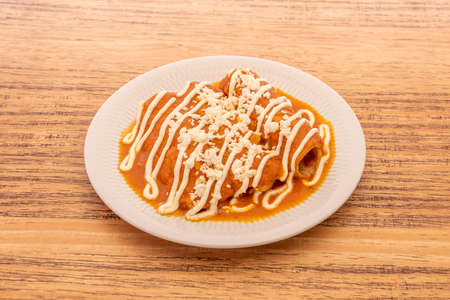 Mexican-style enchiladas dipped in sauce on white plateの写真素材