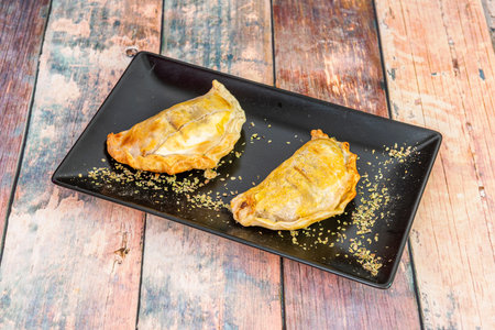 Delicious Argentinian empanadas covered with egg yolk with lots of oregano on a black plate