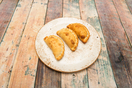Wheat flour patties stuffed with stewed beef on a white plate with coffee with milk color rim on wooden backgroundの写真素材