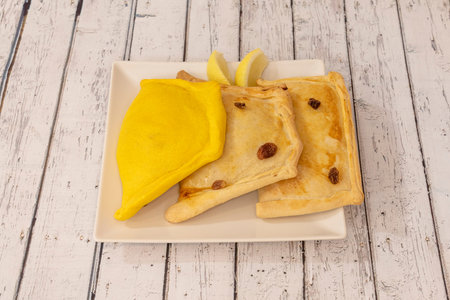 White plate with three Latin American empanadas, one of them with corn dough and some lemon wedges