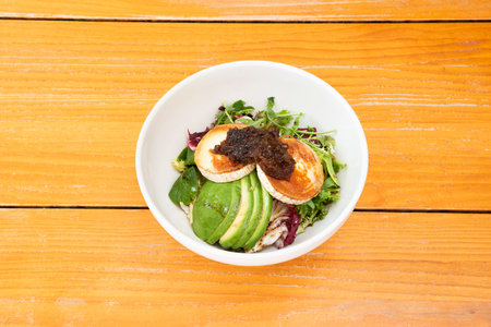 goat cheese salad with avocado, lettuce, arugula and caramelized onion in a white bowl