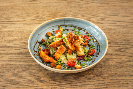 Caesar salad with fresh ingredients, split cherry tomatoes and chives with balsamic vinegar inside blue deep plateの写真素材
