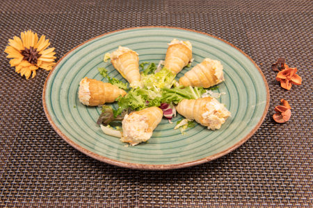 Puff pastry cones stuffed with Russian salad with mayonnaise and cooked potato on a green plate on a...