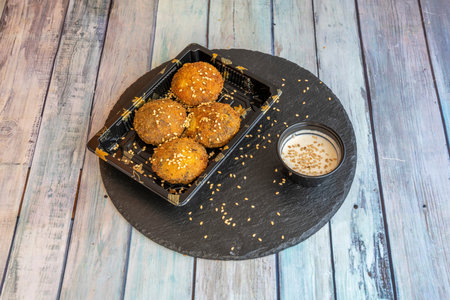 Fried falafel balls with sauce and sesame seeds presented in a plastic container for home delivery