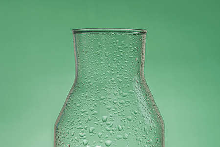 Glass bottle with drops on the surface with green background and low lightの写真素材