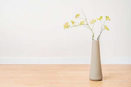 Ornamental long vase with blueberry branches in studio with cream colored walls and oak wood floorの写真素材
