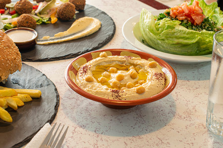Table with various Arabic dishes and the center a clay bowl with chickpea hummus cooked with olive...