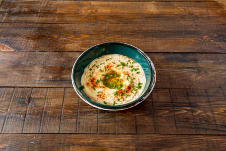 Fantastic Arabic chickpea hummus with olive oil, chopped parsley and paprika powder on the dark wooden table.の写真素材