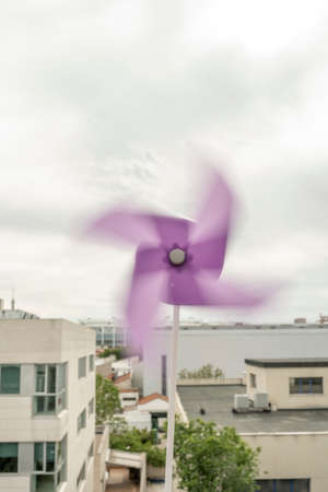 Windmill spinning on cloudy day with cityscape in the backgroundの写真素材