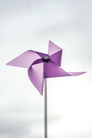 Vertical image in low angle shot of purple pinwheel with background of gray cloudsの写真素材