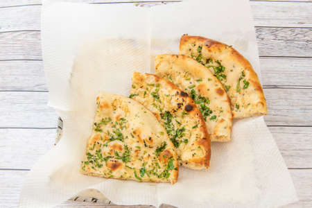 Portions of traditional hindu naan garlic bread on absorbent paper and lots of parsley on white tableの写真素材
