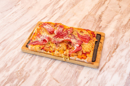 Rectangular pizza of fresh wheat dough with serrano ham and grated cheese on marble tableの写真素材