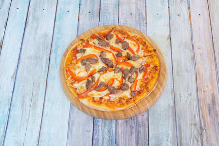 Pizza with pieces of sauteed beef, red peppers, onion and mozzarella cheese gratin made with wheat flour on wooden plateの写真素材