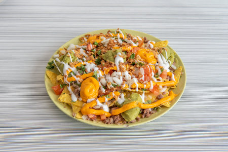 Plate of nachos with guacamole with lots of ingredients to the beast on a green plateの写真素材