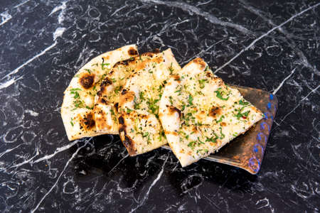Portions of Hindu Naan Garlic Bread with Parsley and Nuts on Black Marble Tableの写真素材