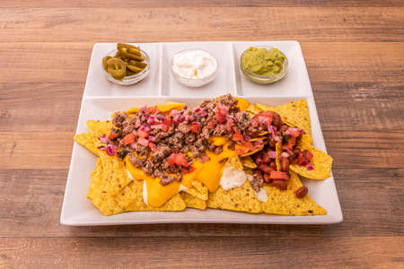 White plate of nachos with guacamole neatly ordered on wooden tableの写真素材