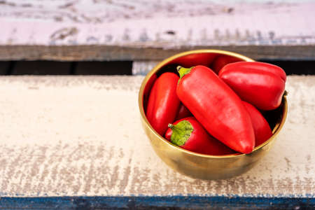 Raw red peppers inside a bowl that is on cream colored wooden boardsの写真素材