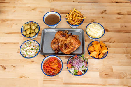 Roast chicken on a metal tray surrounded by all kinds of garnishes served in bowlsの写真素材