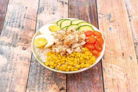 Chicken poke bowl with sweet corn, cherry tomatoes, boiled egg, rice and sesame seedsの写真素材