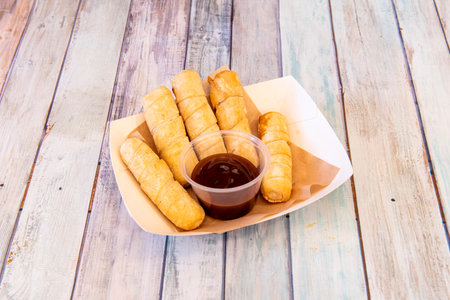 Tray of Venezuelan tequeÃ±os with sweet apple syrup on wooden table