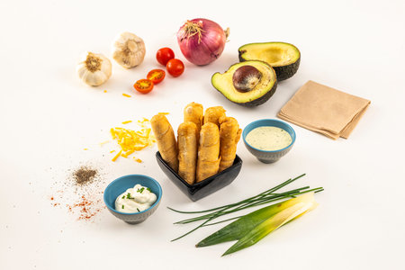 composition with tequeÃ±os, avocados, sauces and vegetables on a white background