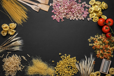 composition with many kinds of pasta, tomatoes and kitchen utensils on black background