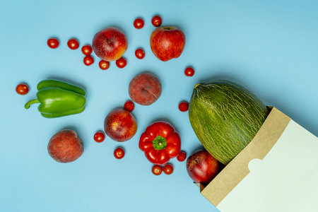 Fruits and vegetables pouring out of an eco-friendly shopping bag on blue background