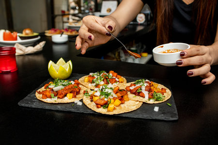 Hand salseado tacos al pastor on a slate plate on the counter of a Mexican restaurant