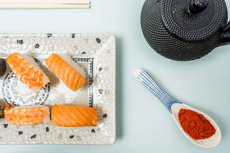 Top view image of paprika on a spoon, black teapot, salmon and crayfish nigiri, chopsticks and pale blue tableの写真素材