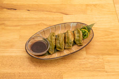 tray of fried vegetable gyozas on the grill with soy sauce on a banana leaf and wooden tableの写真素材