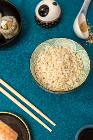 Bowl of white rice with sushi, chopsticks, Chinese blue tablecloth and sesame seeds.の写真素材