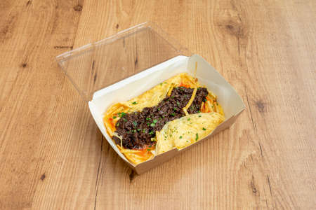 Omelette, fried potatoes and blood sausage with parsley in a container with a plastic lid for home deliveryの写真素材