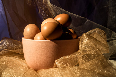 Pink bowl among tulle fabrics with gold glitters filled with fresh raw eggs