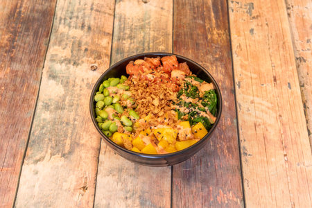Black bowl of Hawaiian poke with Norwegian salmon, crunchy onion, Japanese edamame, African mango...