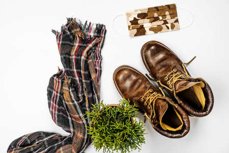 Brown leather hiking boots, camouflage mask, thin scarf and plant in one corner on white studio backgroundの写真素材