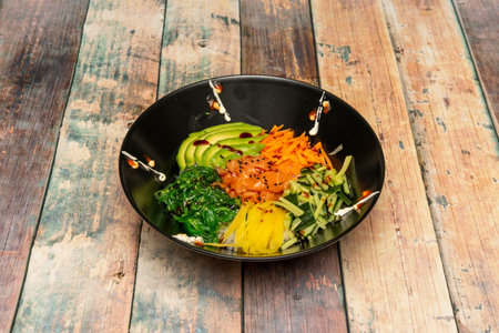 Marinated salmon poke bowl with ripe avocado slices, mango strips, green cucumber strips, wakame...