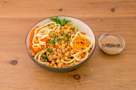 Vegan salad with zucchini noodles, carrot noodles, cooked chickpeas, olive oil, chopped parsley, and sesame poppy seeds in a black bowlの写真素材