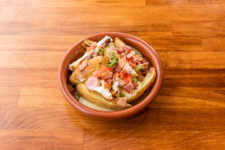 Roasted potato salad with skin, fried bacon in pieces, diced tomatoes with cream cheese on clay potの写真素材