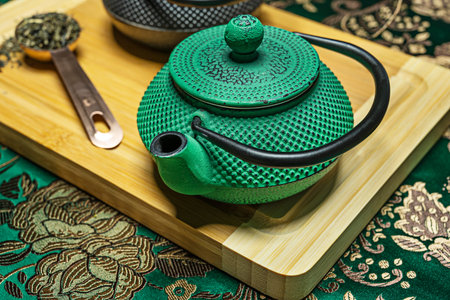 Closeup of traditional Chinese cast iron green teapot with green cloth background, copper saucepan...