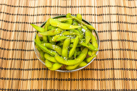 Glass bowl with metallic edge filled with edamame with salt flakes. Immature soybeans on bambooの写真素材