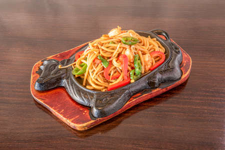 Stir-fried udon noodles with vegetables and peeled shrimp cooked by a Chinese chef and served on a boiling cast iron trayの写真素材