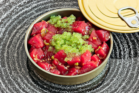 marinated red tuna tartare with sesame seeds, onion and fish roe in a plate that resembles a can of...