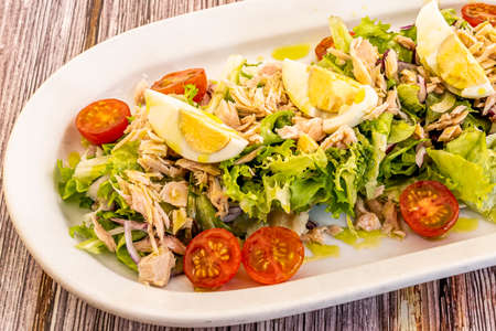 Mixed salad with boiled egg, preserved bonito del norte, split cherry tomatoes, lettuce and escarole, red onion and Spanish extra virgin olive oilの写真素材