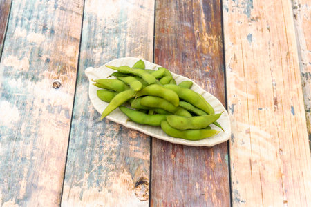Small leaf shaped tray holding portion of Asian edamame in pod with some sea salt on wooden tableの写真素材