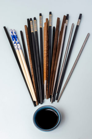 Chinese chopsticks of different textures, colors and materials, a blue bowl with soy sauce on a sky blue background